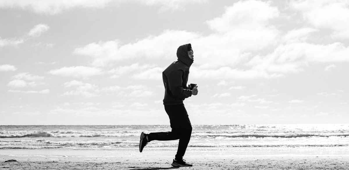 Silhouette of a jogger running along La Lucila del Mar beach, captured in monochrome.